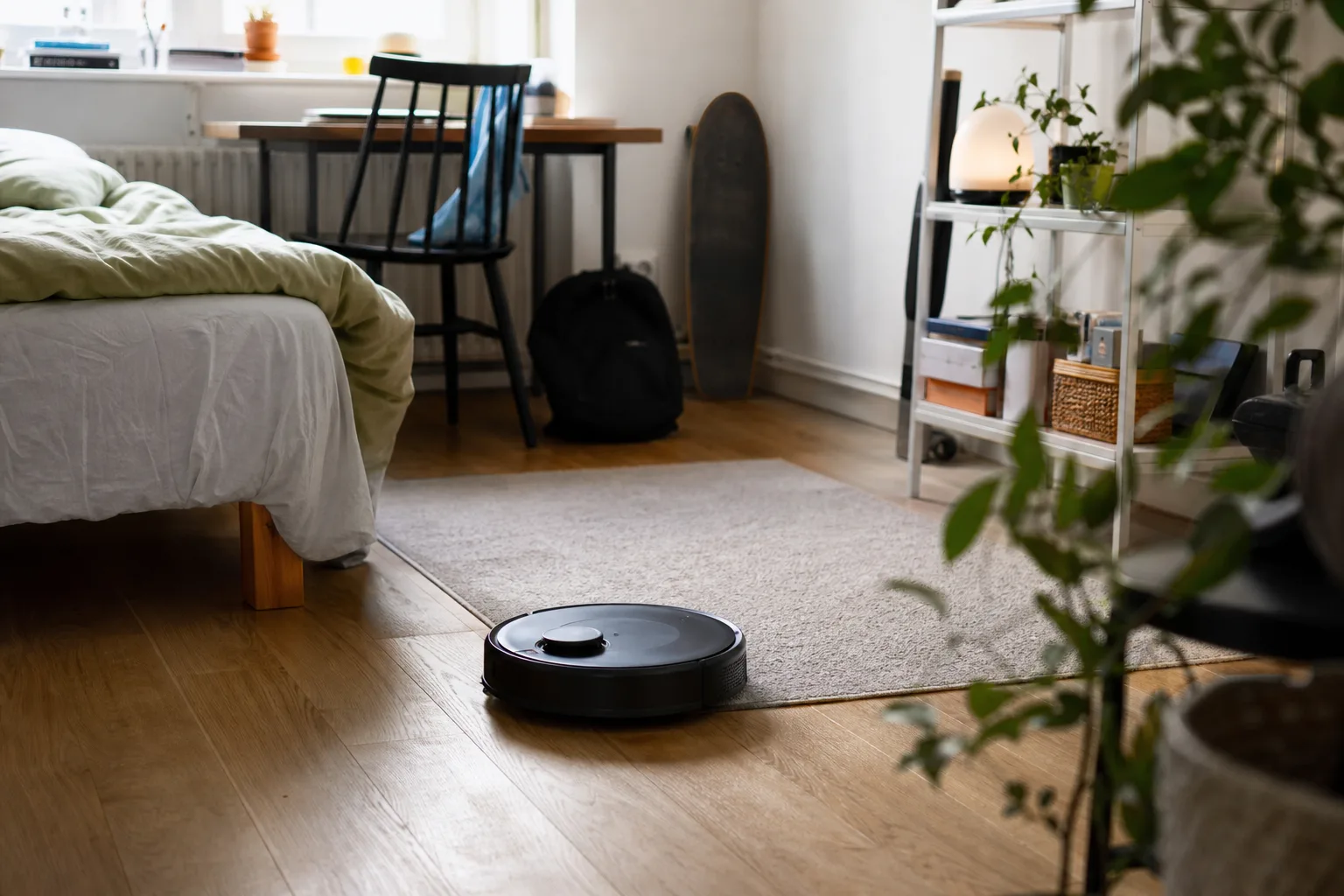 Kompakt robotdammsugare som städar ett litet svenskt studentrum med hårt golv och en enkel matta